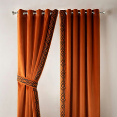 Pair of orange curtains with decorative black patterns on a plain background